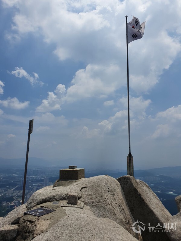 불암산 정상과 펄럭이는 태극기. 불암산 정상에 올라가려면 밧줄을 잡고 바위를 약간 올라가야 한다. 불암산 정상에는 측량점과 국기봉이 설치되어 있고 국기봉 끝에 태극기가 세찬 바람에 펄럭이고 있다.